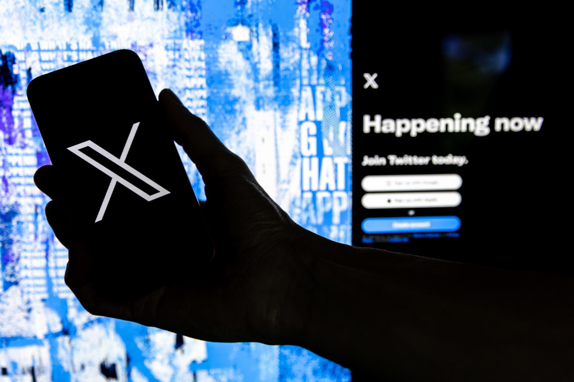Fotografía de archivo que muestra un usuario mientras sostiene un teléfono móvil que muestra el logotipo 'X' frente a la página principal de Twitter en Los Ángeles, California (EE.UU.). EFE/EPA/ETIENNE LAURENT
