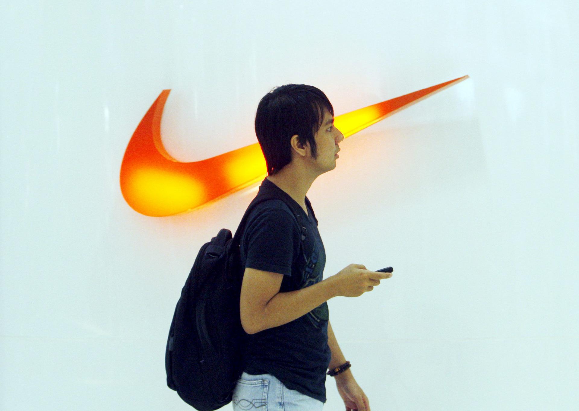 Fotografía de archivo en la que se registró a un hombre al pasar por delante del logo de la compañía de calzado y ropa deportiva Nike. EFE/Mast Irahm