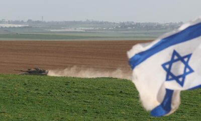 Un tanque israelí pasa junto a una bandera nacional de Israel en la frontera con la Franja de Gaza. EFE/EPA/ABIR SULTAN