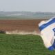 Un tanque israelí pasa junto a una bandera nacional de Israel en la frontera con la Franja de Gaza. EFE/EPA/ABIR SULTAN