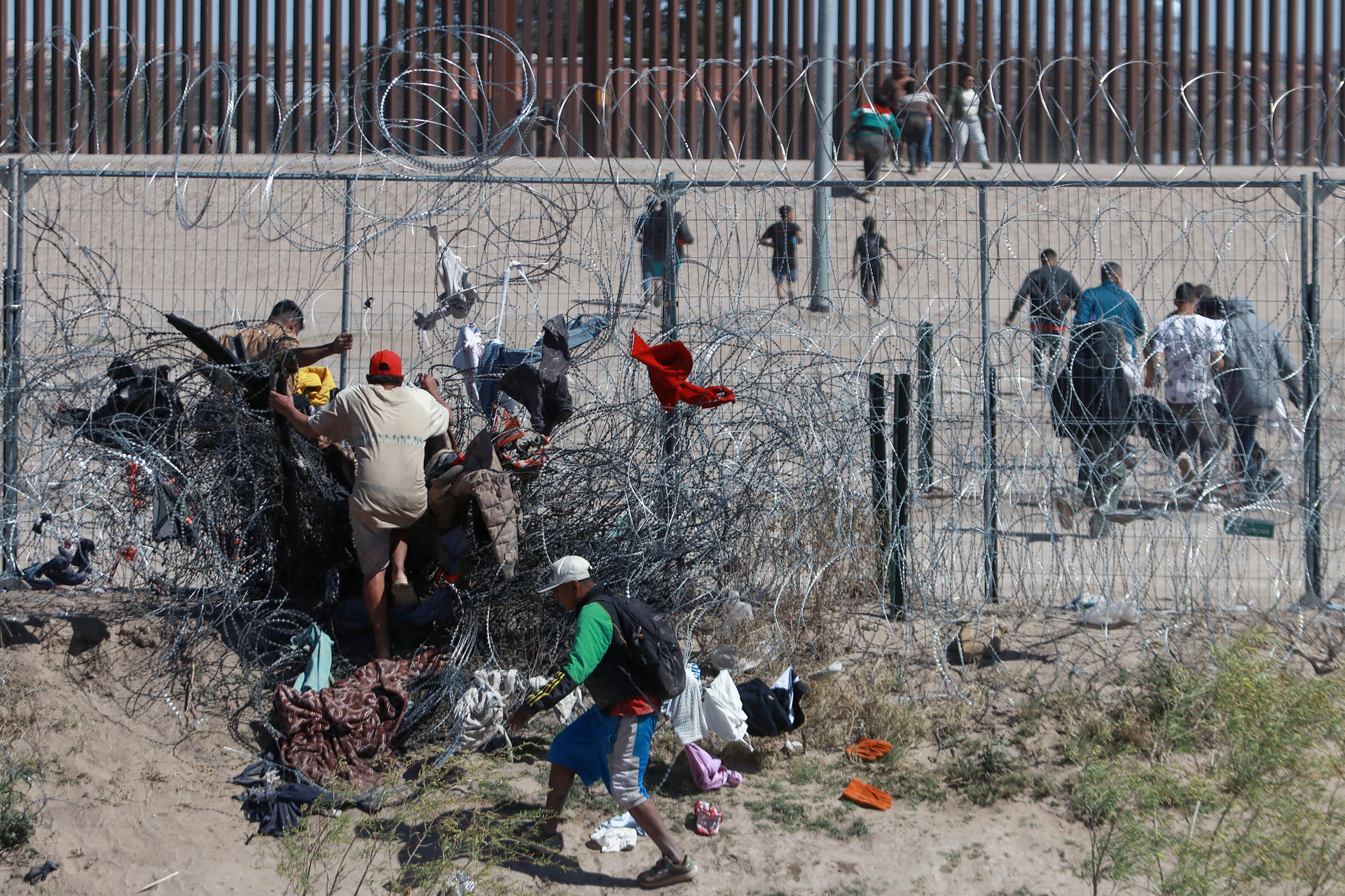 Migrantes cruzan una alambrada de navajas y púas, en la frontera que divide a México de los Estados Unidos en Ciudad Juárez (México). Fotografía de archivo. EFE/Luis Torres