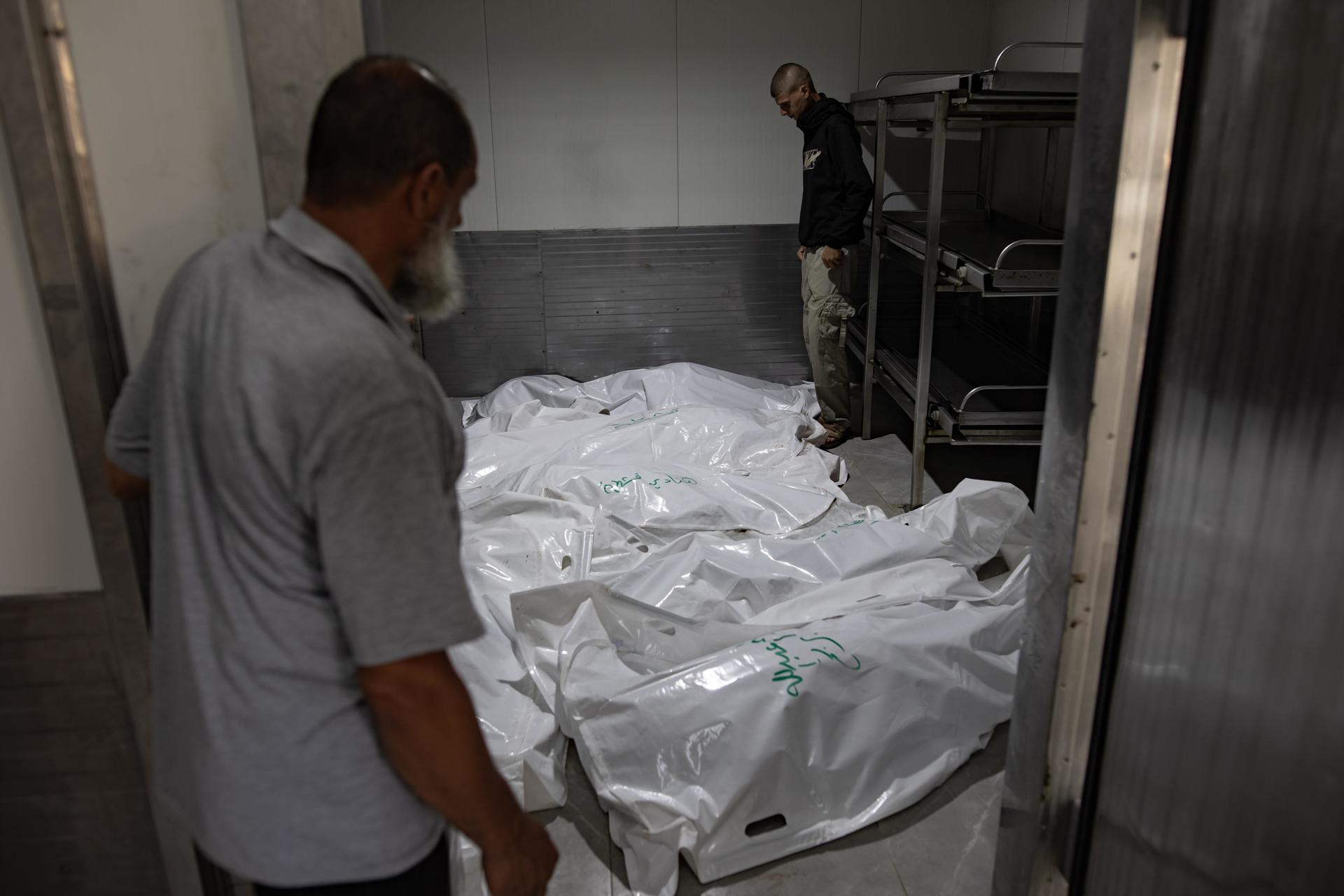 Dos palestinos miran los cadáveres envueltos en bolsas de plástico en la morgue del Hospital Europeo tras un ataque aéreo israelí en Jan Yunis, en el sur de la Franja de Gaza, el 6 de junio de 2024. EFE/EPA/HAITHAM IMAD