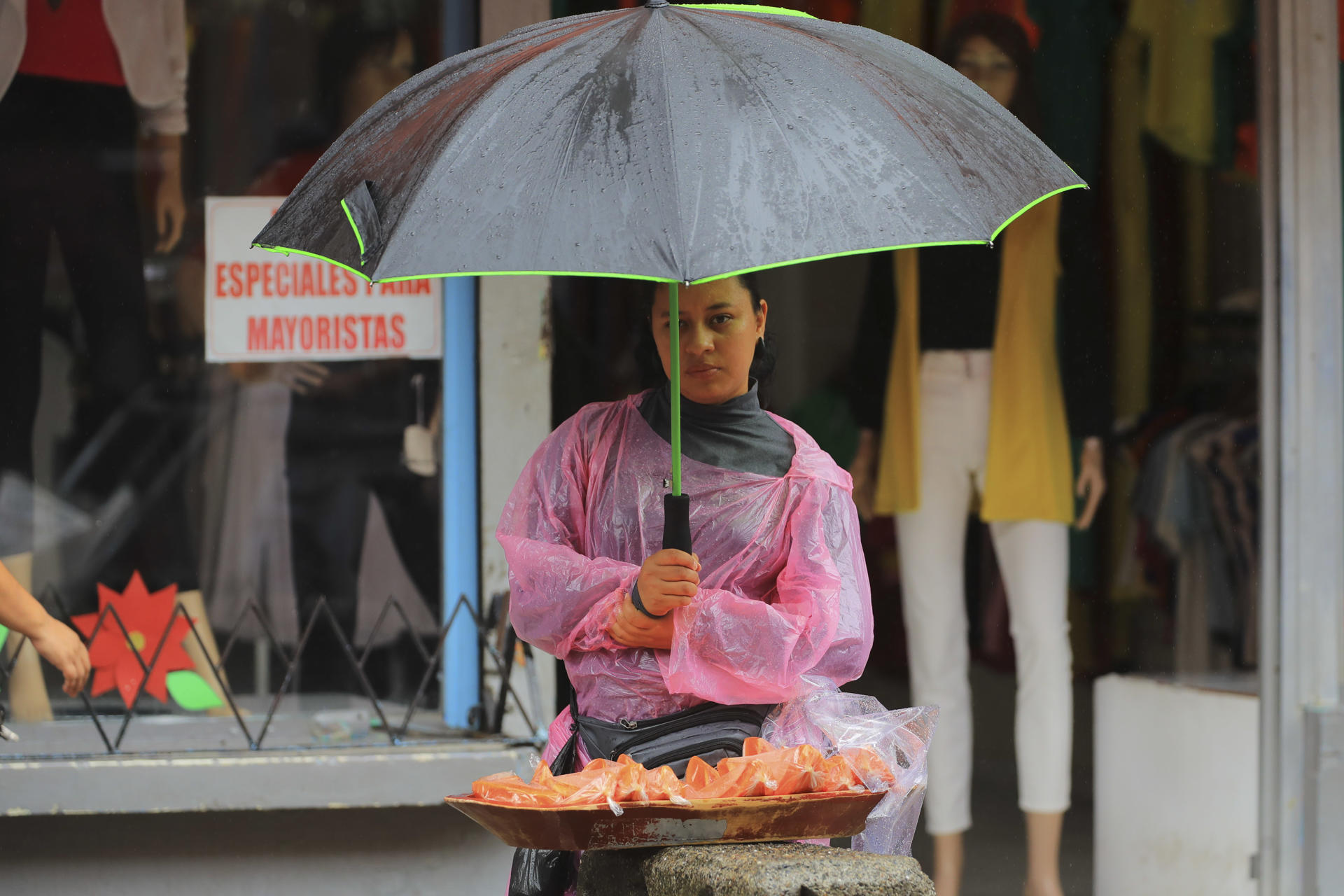 Una muer se protege de la lluvia mientras vende frutas, este lunes en Tegucigalpa (Honduras). EFE/ Gustavo Amador