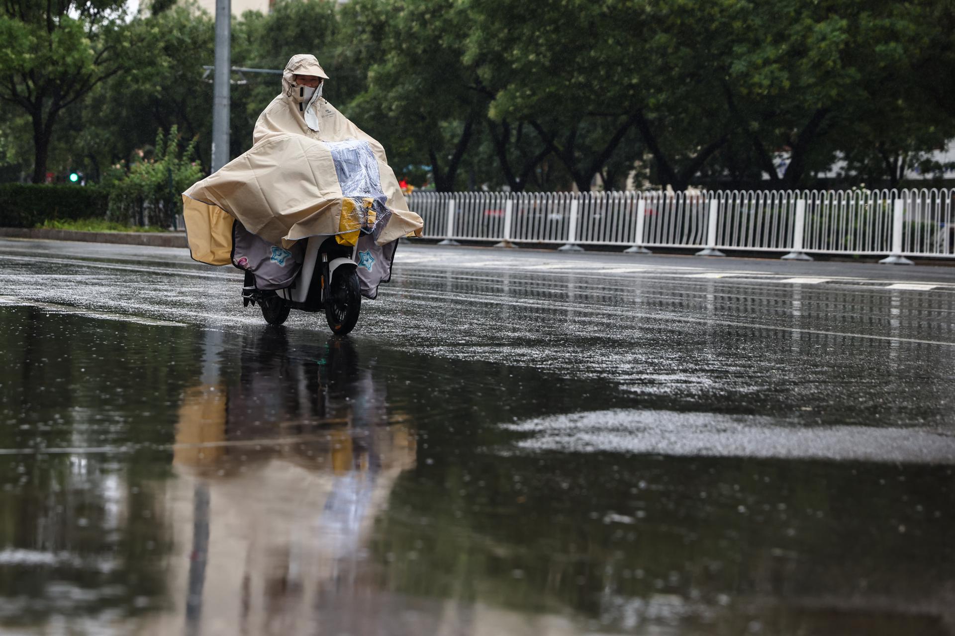 Una mujer anda en scooter durante una fuerte lluvia, en una calle de Beijing (China), el 30 de julio de 2024. El Observatorio Meteorológico Central siguió emitiendo una alerta naranja por tormenta para el martes. EFE/EPA/Wu Hao