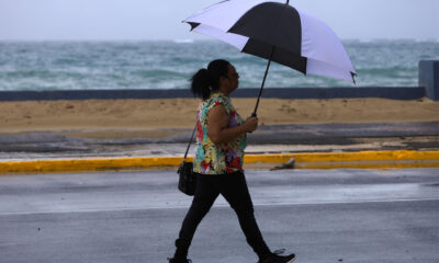 Una mujer se protege de la lluvia con una sombrilla frente a la Playa de Ocean Park, en San Juan (Puerto Rico). EFE/ Thais Llorca