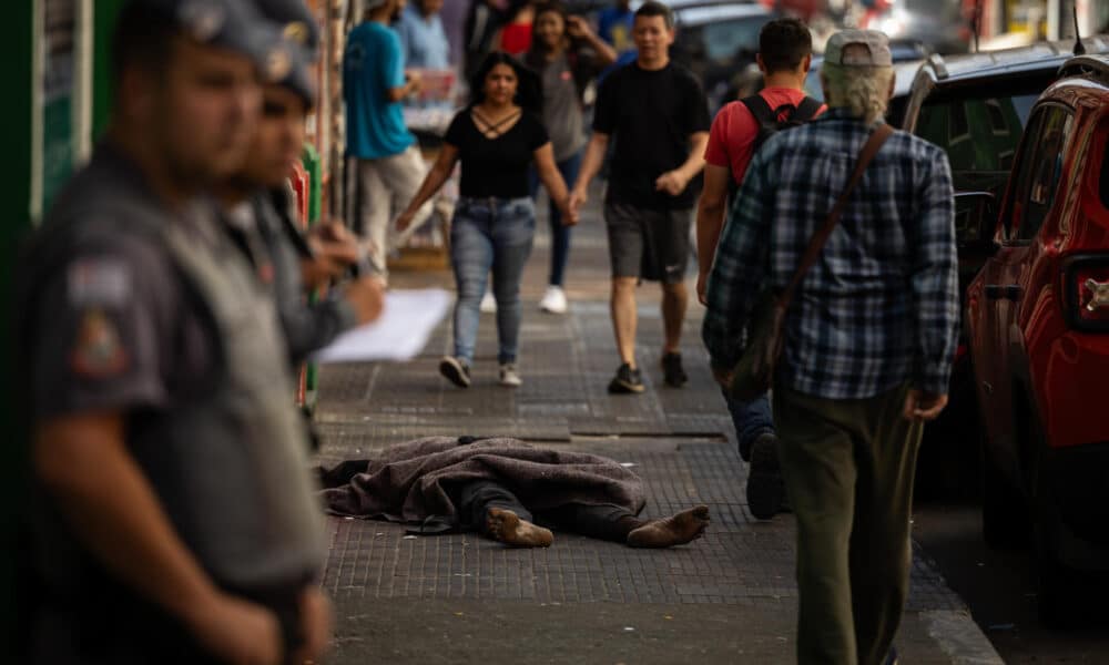 Fotografía de archivo en donde se ve a una persona sin hogar mientras duerme entre compradores y policías en São Paulo (Brasil). EFE/ Isaac Fontana