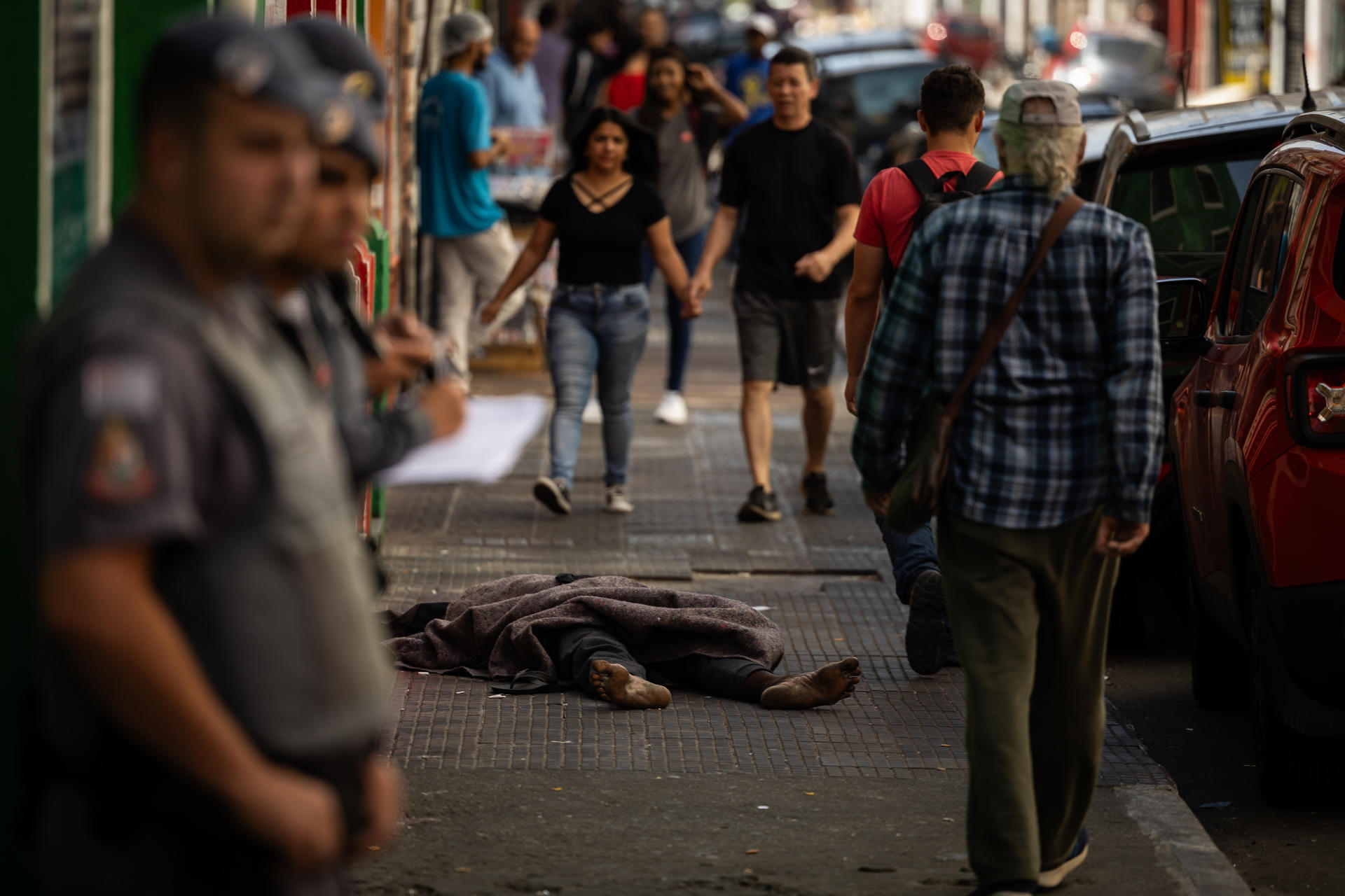 Fotografía de archivo en donde se ve a una persona sin hogar mientras duerme entre compradores y policías en São Paulo (Brasil). EFE/ Isaac Fontana