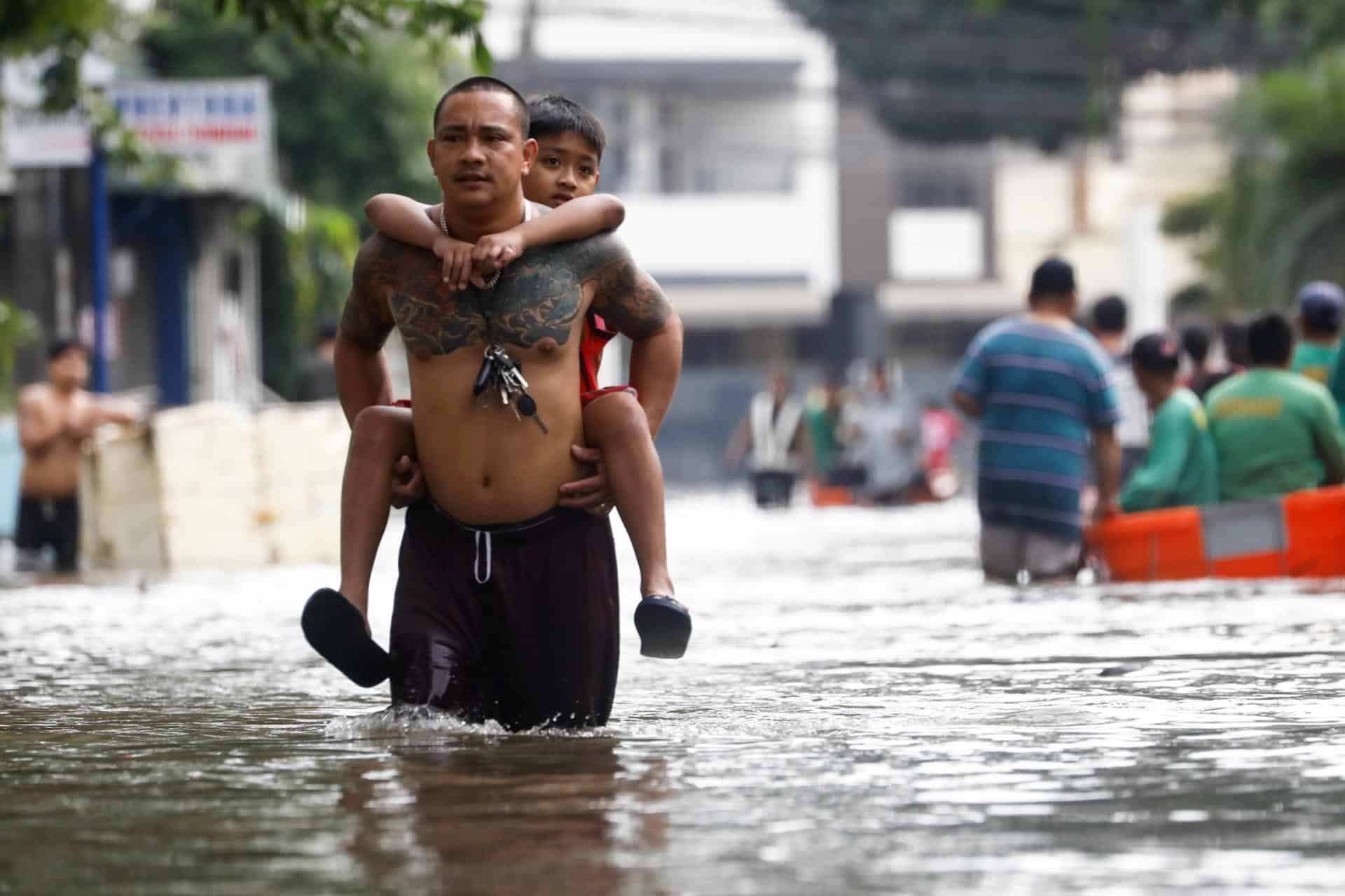 Un hombre lleva a hombros a su hijo este viernes en una calle inundada en la localidad de Cainta, unos 30 kilómetros al este de Manila, tras el paso de la tormenta Trami por el norte de Filipinas. EFE/EPA/ROLEX DELA PENA