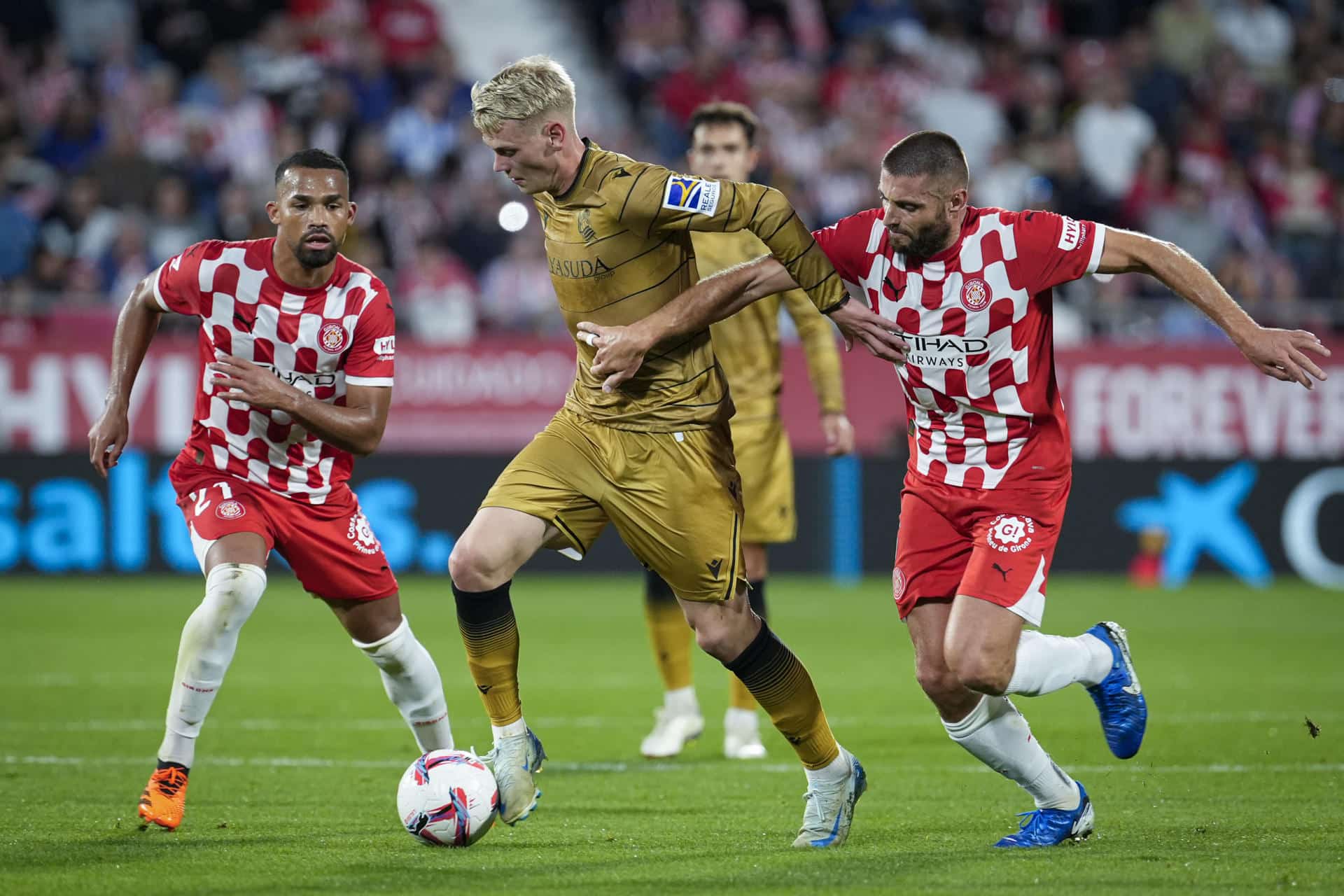 El delantero de la Real Sociedad Orri Óskarsson (c) trata de escapar de David López (d), del Girona, durante el partido de LaLiga EA Sports que Girona FC y Real Sociedad disputaron en el estadio municipal de Montilivi. EFE/David Borrat