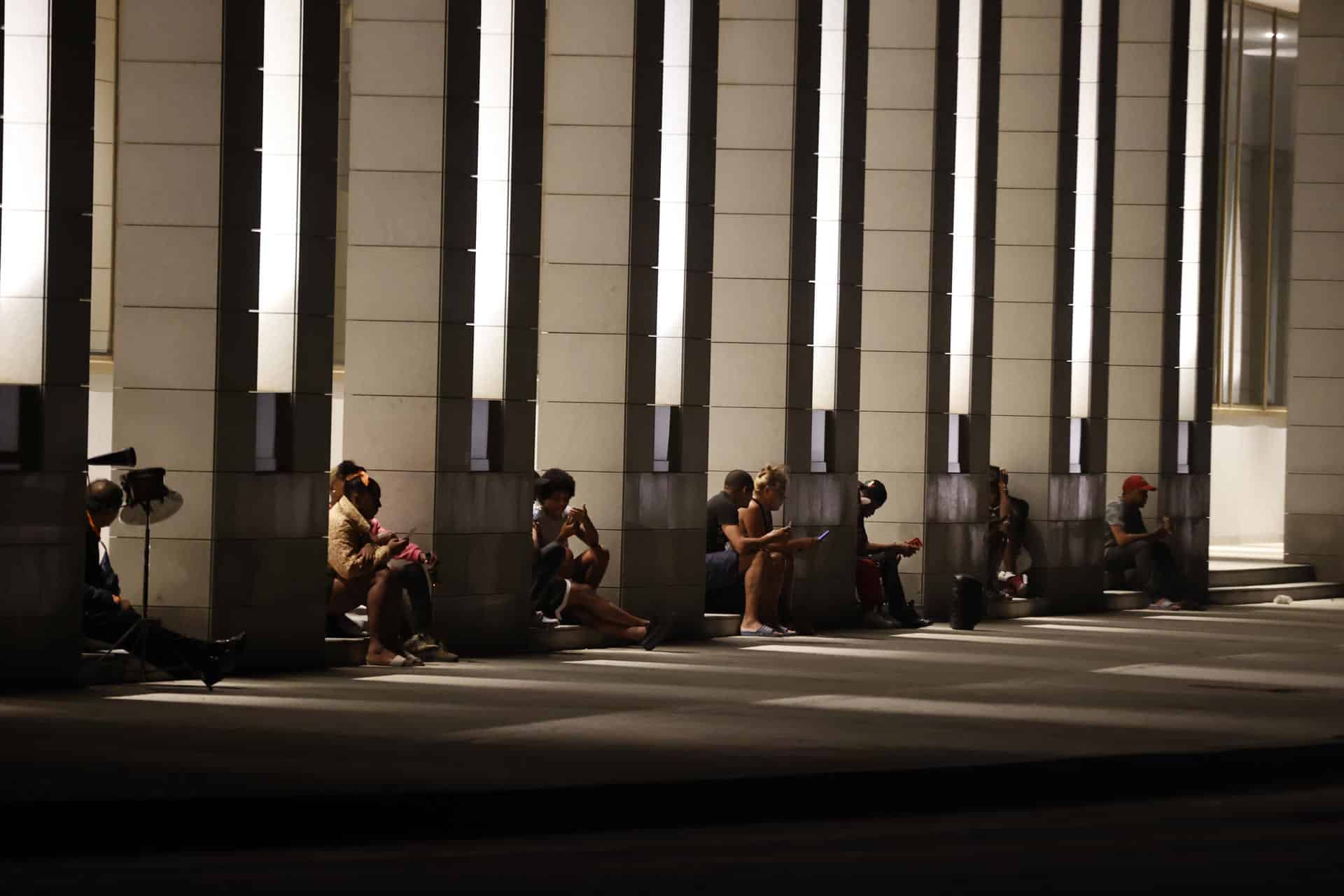 Personas revisan sus teléfonos celulares en el portal de un hotel con electricidad por las plantas eléctricas en La Habana (Cuba). EFE/ Ernesto Mastrascusa