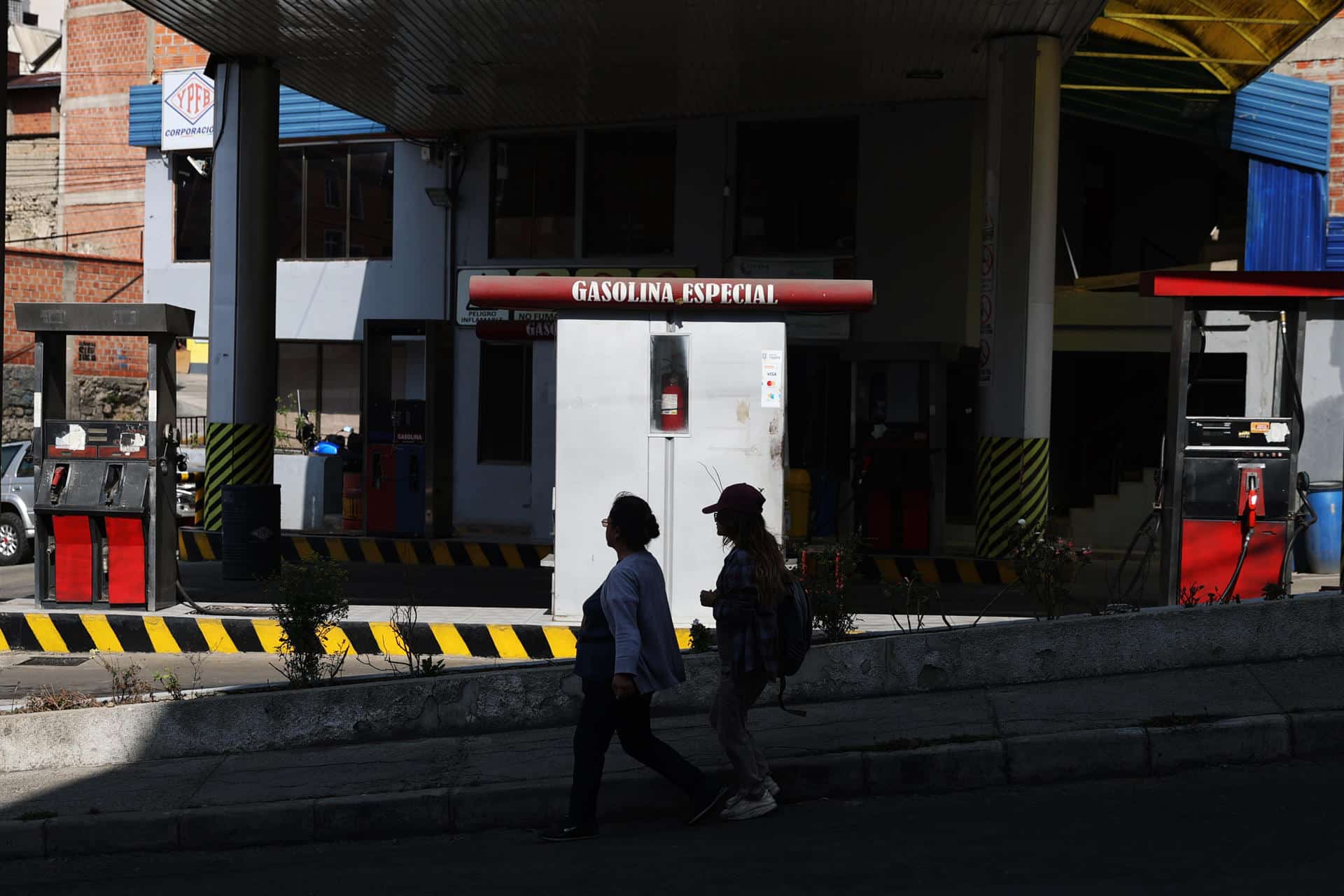 Mujeres caminan delante de una estación de servicio cerrada por falta de combustible este miércoles, en La Paz (Bolivia). EFE/Luis Gandarillas