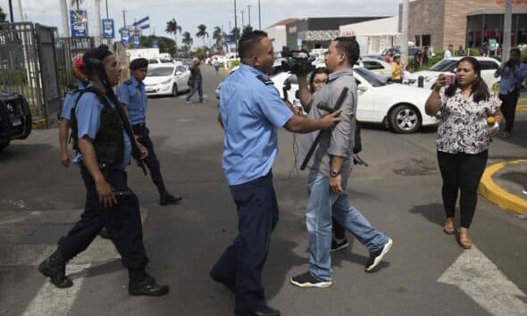 Fotografía de archivo del 12 de diciembre de 2019, en la que se observa a un agente de la Policía Nacional (c) obstruyendo el paso a un camarógrafo durante una protesta que exige la liberación de presos políticos, en Managua (Nicaragua).EFE/STR