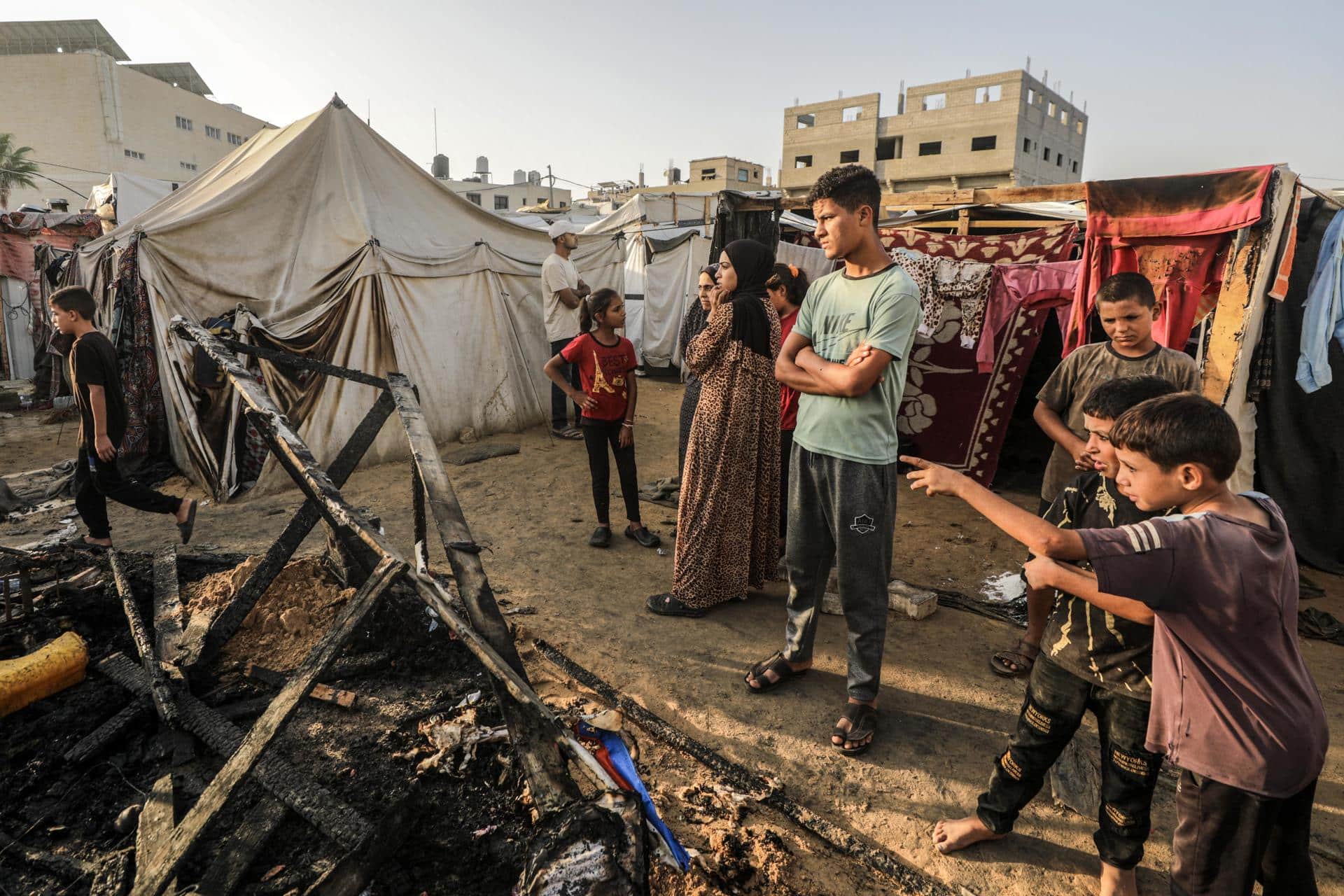 Niños ante los restos calcinados de unas tiendas en el campamento de Deir al Balah. EFE/EPA/MOHAMMED SABER