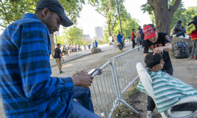 Fotografía que muestra un inmigrante mientras le corta el cabello a otro afuera del refugio de Randall Island en Nueva York (EE.UU.). EFE/Angel Colmenares