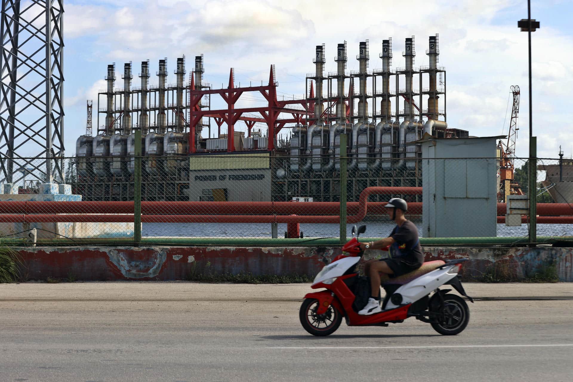 Un hombre en una moto eléctrica pasa frente a una de las plantas de generación eléctrica que permanece este domingo, en el puerto de La Habana (Cuba). EFE/ Ernesto Mastrascusa