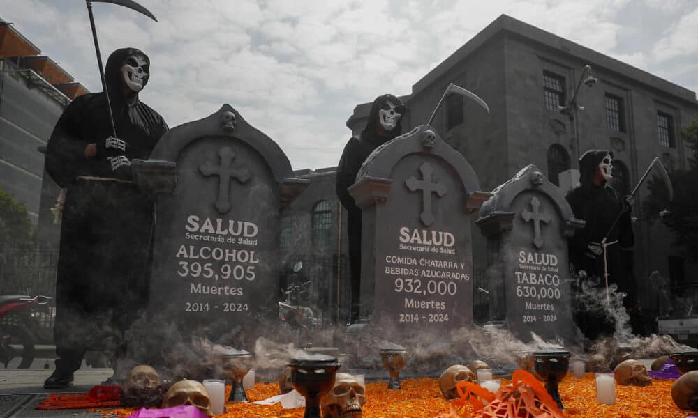 Miembros de organizaciones sociales disfrazados de calaveras posan junto a una ofrenda con esquelas que muestran presuntas cifras de muertes por alcohol, comida chatarra y bebidas azucaradas y tabaco en los últimos 10 años, que colocaron frente a la Secretaría de Salud este jueves, en la Ciudad de México (México). EFE/ Isaac Esquivel