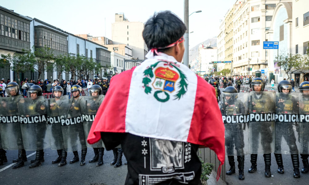 Un manifestante sostiene una bandera de Perú frente a miembros de la policía durante una protesta cerca al Congreso de la República este jueves, en Lima (Perú). EFE/ STR