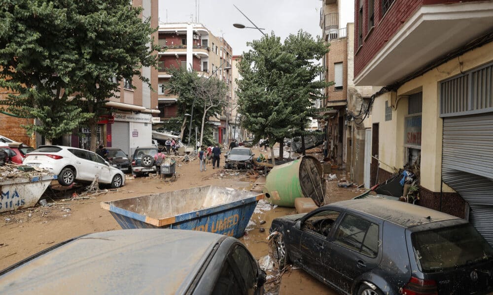 Unas personas caminan por una calle cubierta de lodo y llena de coches amontonados tras las intensas lluvias por la fuerte dana que afecta especialmente el sur y el este de la península ibérica, este miércoles en Valencia. EFE/Manuel Bruque