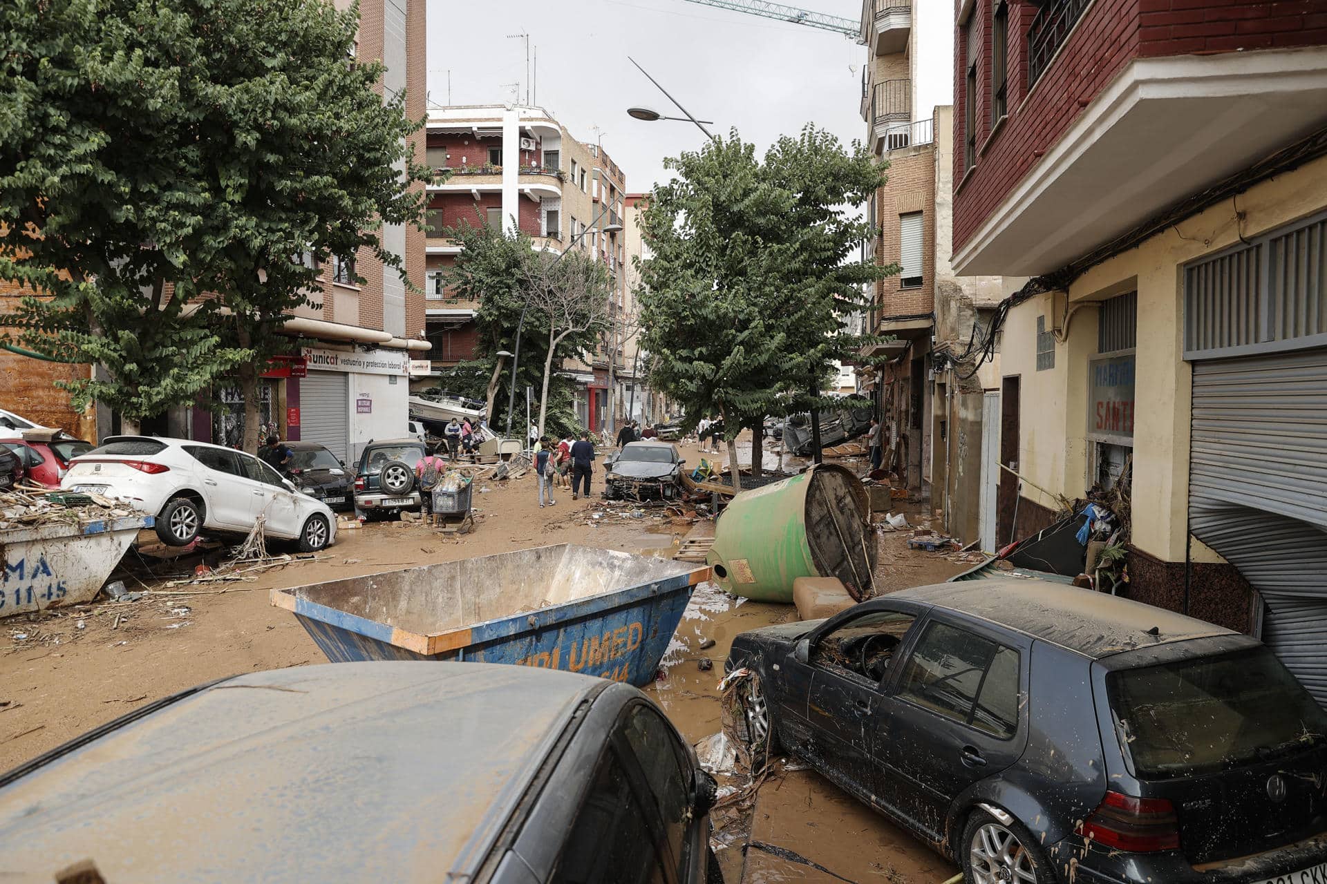 Unas personas caminan por una calle cubierta de lodo y llena de coches amontonados tras las intensas lluvias por la fuerte dana que afecta especialmente el sur y el este de la península ibérica, este miércoles en Valencia. EFE/Manuel Bruque