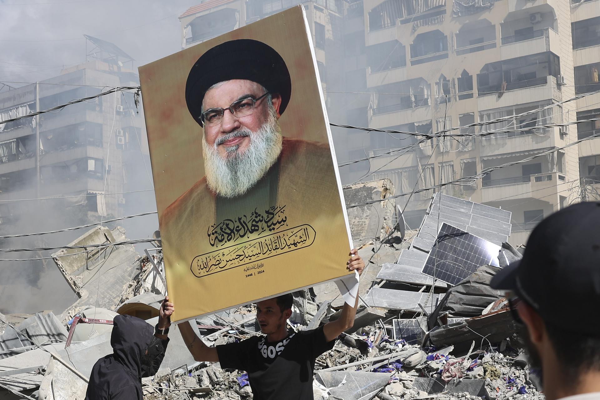 Un partidario de Hizbulá sostiene una pancarta con la imagen del líder del grupo chií libanés, Hasán Nasrala, asesinado por Israel, junto a los escombros de un edificio completamente destruido en Dahye, un suburbio del sur de Beirut, Líbano, el 2 de octubre de 2024. EFE/EPA/JOAO RELVAS