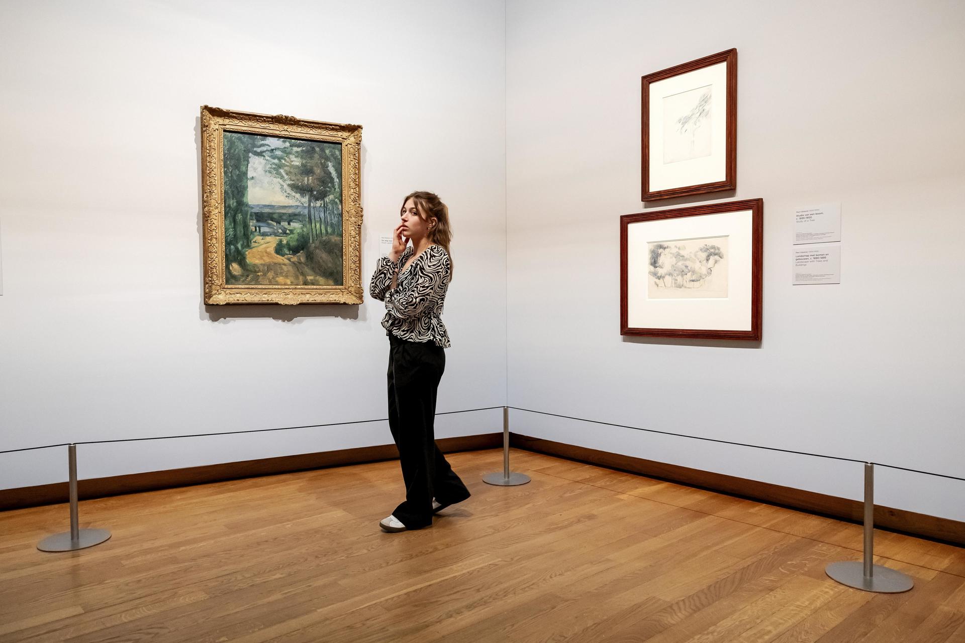 Una mujer contempla las obras 'El camino del lago' y 'Estudio de un árbol y paisaje con árboles y edificios' de Paul Cezanne, de la nueva exposición Vive l'impressionnisme! en el Museo Van Gogh de Ámsterdam, 09 de octubre de 2024. La exposición muestra las mejores obras impresionistas francesas de colecciones holandesas. (Países Bajos; Holanda) EFE/EPA/ROBIN VAN LONKHUIJSEN