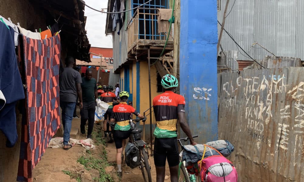 El grupo de la caravana de bicicletas atravesando una de las callejuelas de Kibera, un asentamiento informal situado en Nairobi, para llegar hasta la casa de la ONG Kings and Queens of Kibera. EFE/ Cristina Ondó Nieto