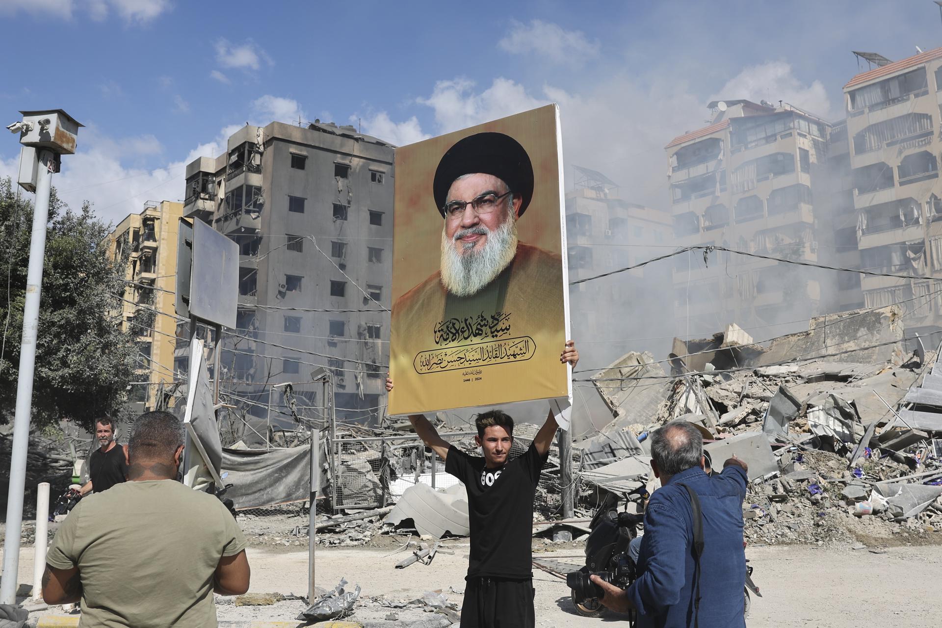 Un partidario de Hizbulá sostiene este miércoles una pancarta con la imagen de Hassan Nasrallah, junto a los escombros de un edificio completamente destruido en Dahieh, un suburbio del sur de Beirut controlado por Hizbulá. EFE/EPA/JOAO RELVAS