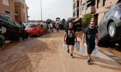 Varias personas con botellas de agua caminan entre los vehículos destrozados en la región valenciana de Paiporta a causa de las fuertes lluvias causadas por la DANA. EFE/Manu Bruque