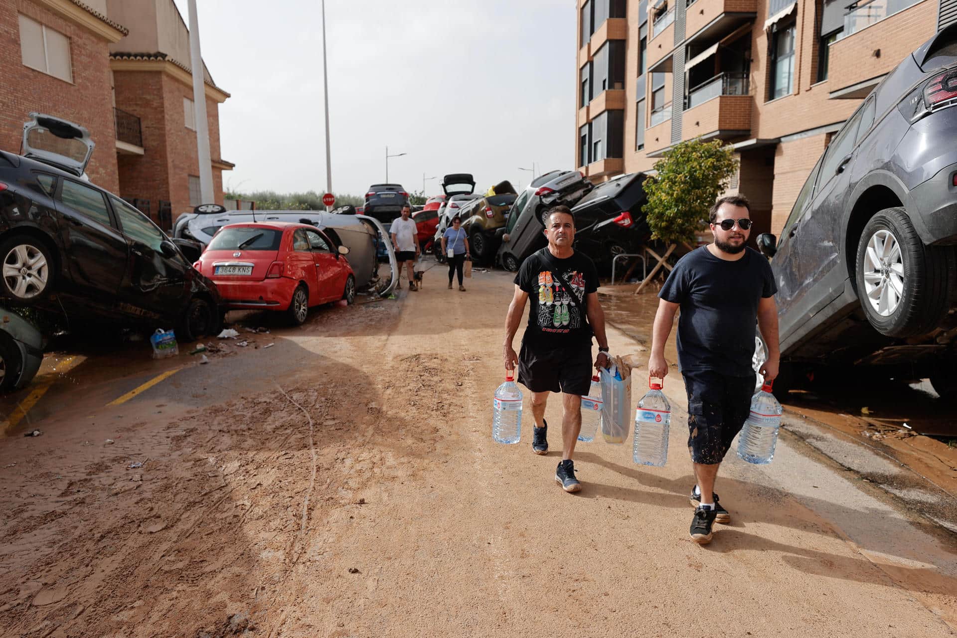 Varias personas con botellas de agua caminan entre los vehículos destrozados en la región valenciana de Paiporta a causa de las fuertes lluvias causadas por la DANA. EFE/Manu Bruque