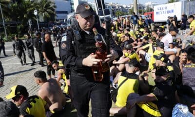 Un integrante de la policía incauta botellas con licor a los fanáticos del Peñarol de Uruguay, luego de ser detenidos en la playa de Pontal en Río de Janeiro. EFE/ André Coelho