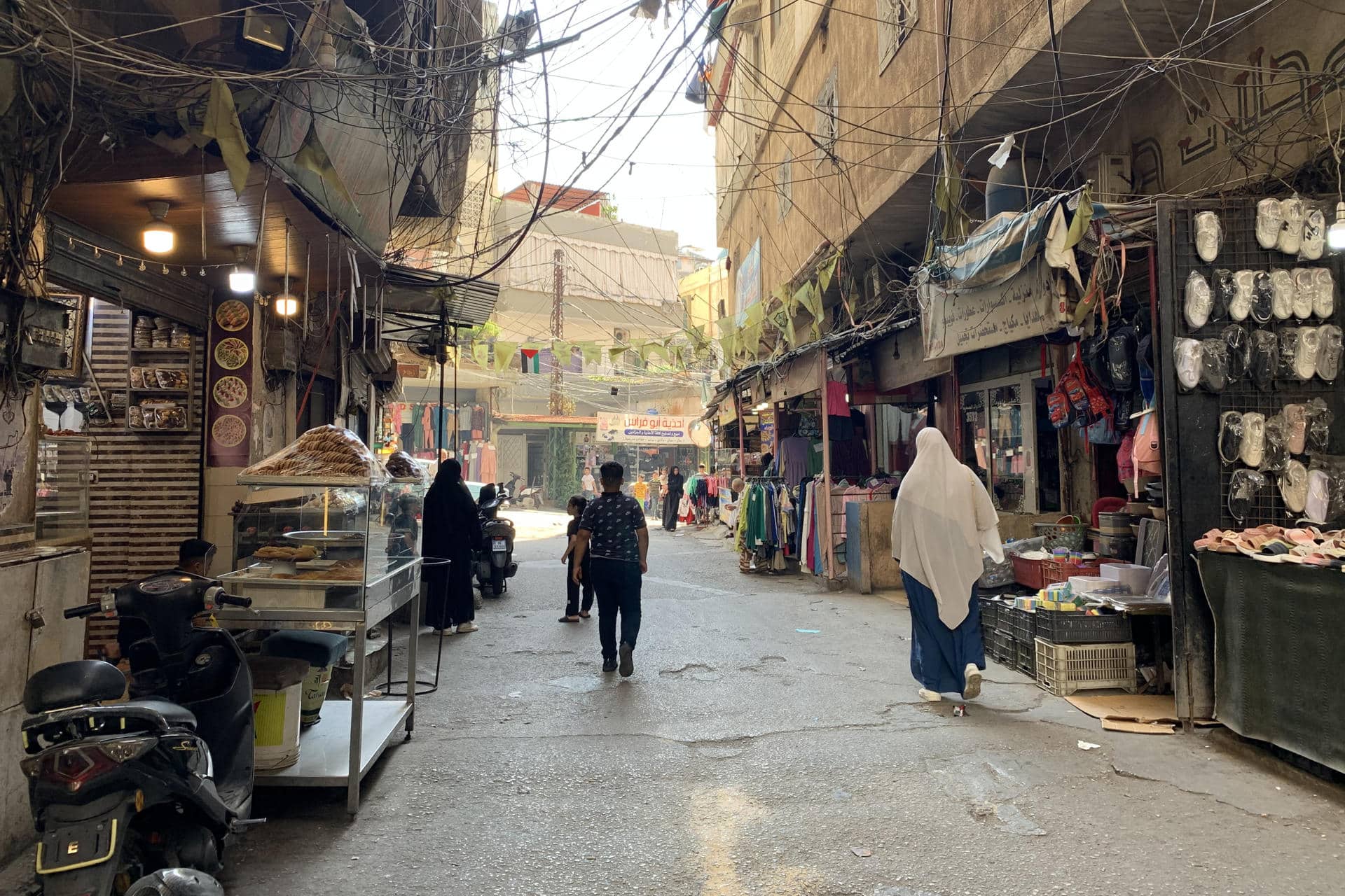 Transeúntes caminan por una calle del campo de refugiados palestinos de Beddawi, en el norte del Líbano, este miércoles. La población del campo de refugiados palestinos de Beddawi no se esperaba que sus laberínticas callejuelas copadas por marañas de cables eléctricos fuesen a ser objetivo de un bombardeo israelí como el del pasado sábado, el primero en el norte del Líbano en un año de violencia. EFE/ Noemí Jabois