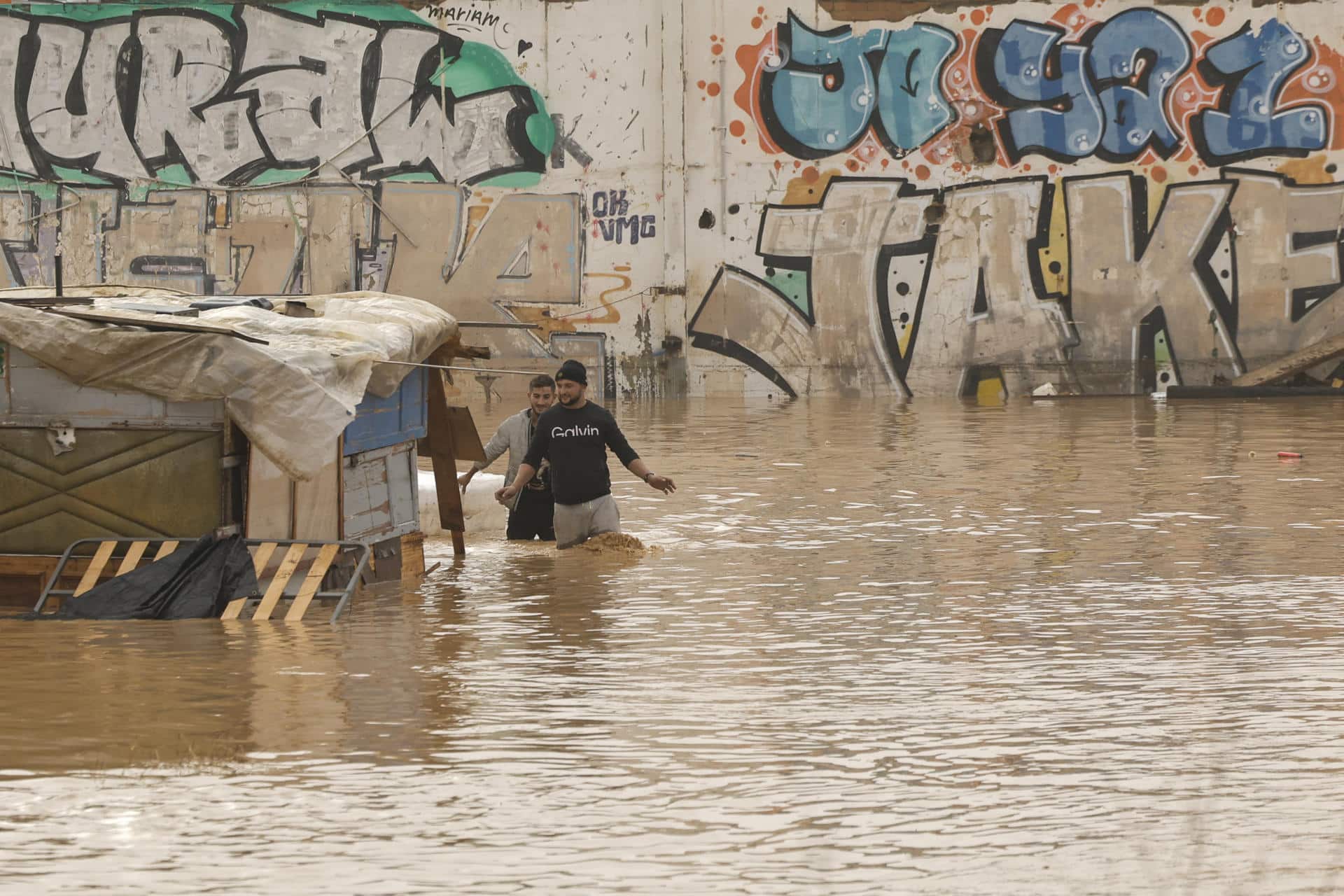 GRAFCVA3847. VALENCIA, 30/10/2024.- Dos personas vadean un terreno de chabolas inundado junto a la V-30 a causa de las lluvias torrenciales de las últimas horas. EFE/Biel Aliño