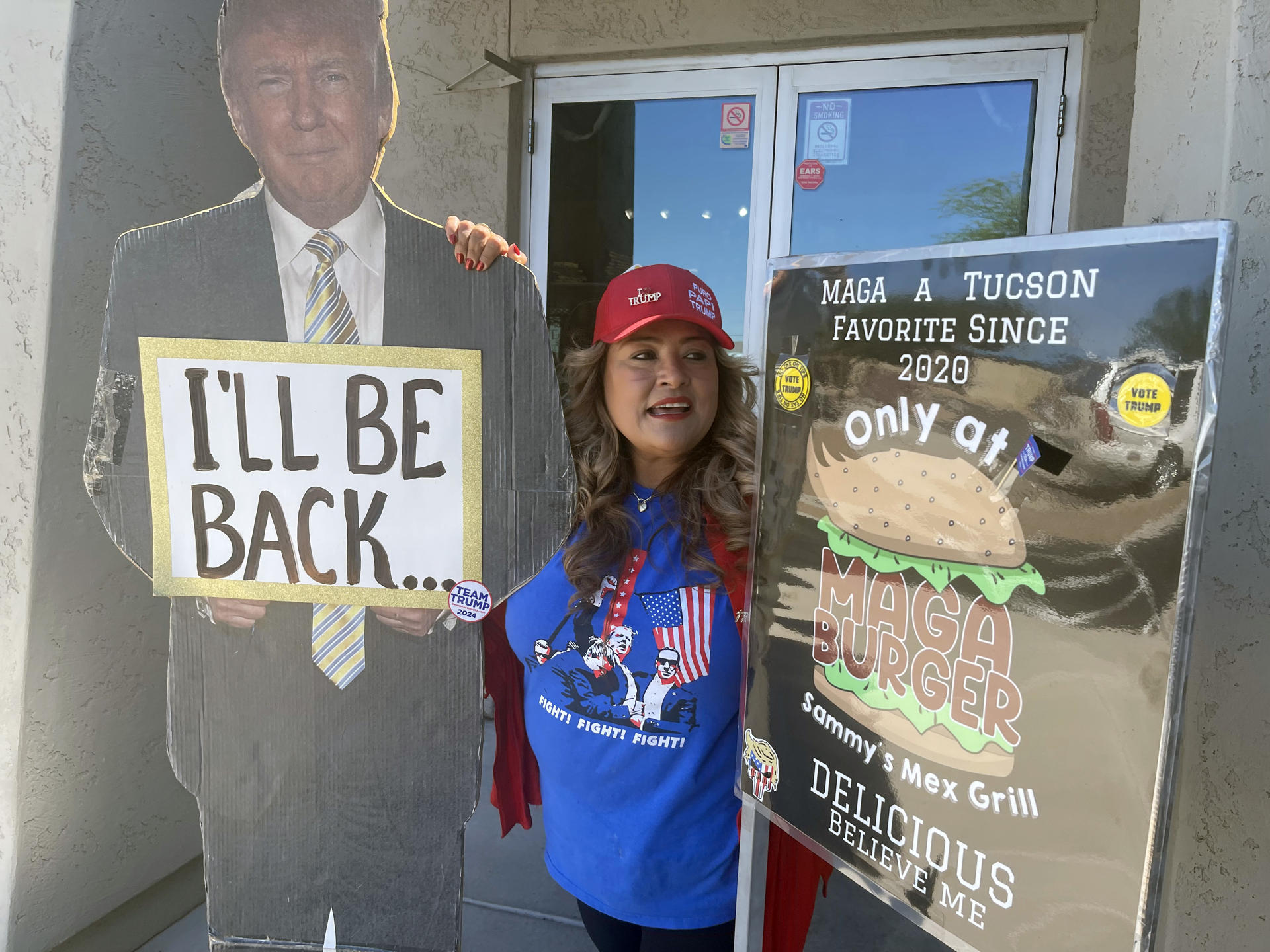 Fotografía del 28 de septiembre de 2024 de la mexicana Betty Rivas, posando junto a los carteles a favor del expresidente republicano Donald Trump, uno con su imagen que dice 'I'll be back' (Volveré) y otro de su hamburguesa 'MAGA Burguer', bautizada con las siglas de la campaña de Trump 'Make America Great Again' (Hacer EEUU grande de nuevo), en la puerta de su restaurante Sammy's Mexican Grill, en Catalina, Arizona (Estados Unidos). EFE/ Ana Milena Varón