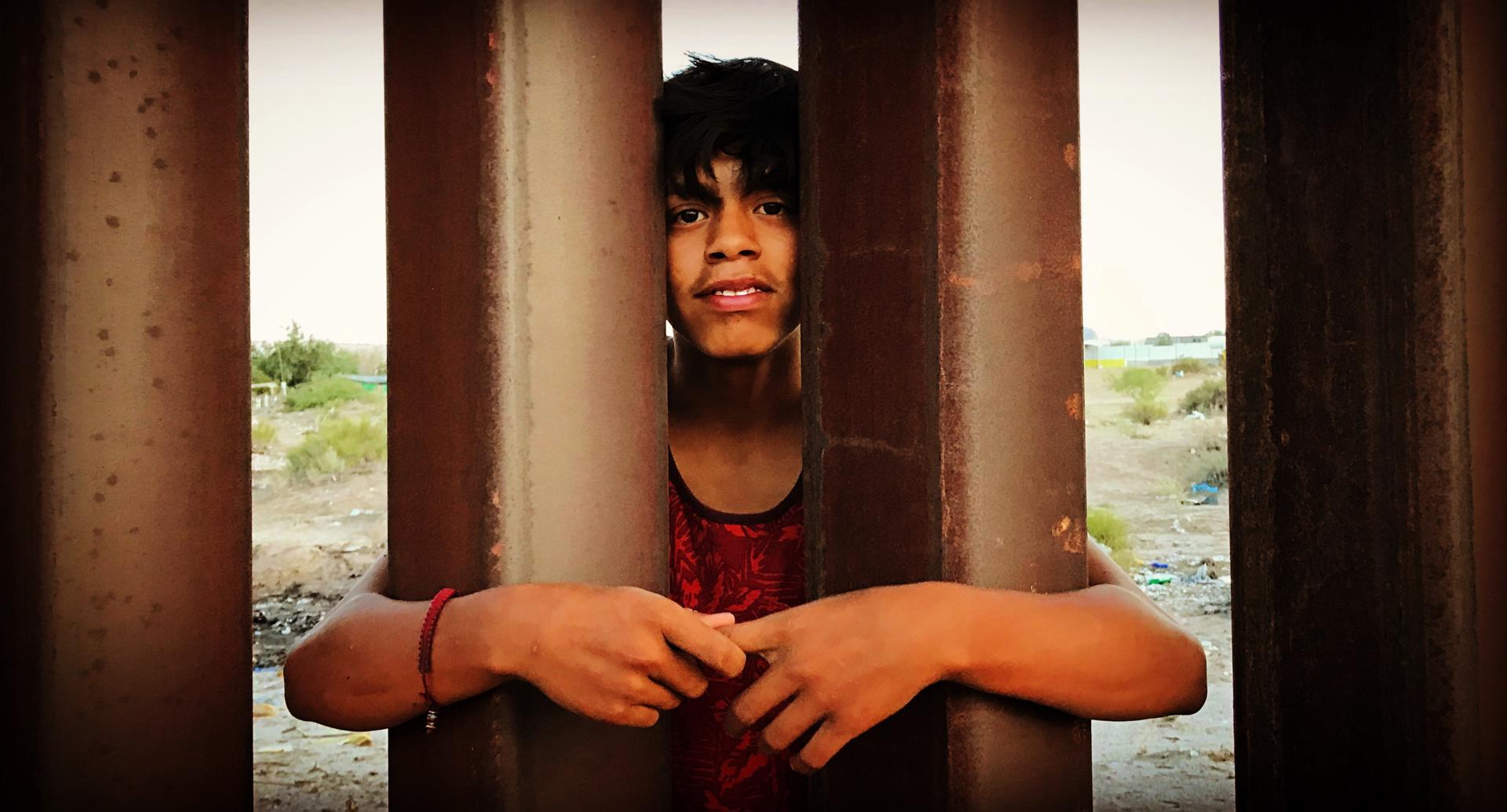 Fotograma cedido por Juan Hernández donde aparece un joven mexicano aferrado a la valla fronteriza, durante una escena del documental 'Frontera adentro' que habla sobre "el complejo industrial fronterizo", en referencia al uso de miles de millones de dólares en la militarización de la frontera y el establecimiento de docenas de centros de detención y uso de tecnología de punta. La cineasta estadounidense Pamela Yates, directora del documental 'Frontera adentro', dijo a EFE que quiere enseñar con su nuevo filme lo que ella aprendió del "negocio" que es la inmigración irregular en EE.UU. y lo valientes que son los migrantes que lo han denunciado. EFE/Juan Hernández