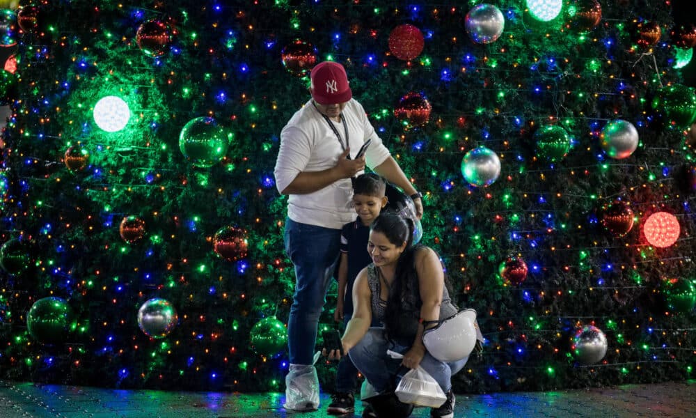 Personas se toman una fotografía junto a un árbol navideño este lunes, en Caracas (Venezuela). EFE/ Miguel Gutiérrez