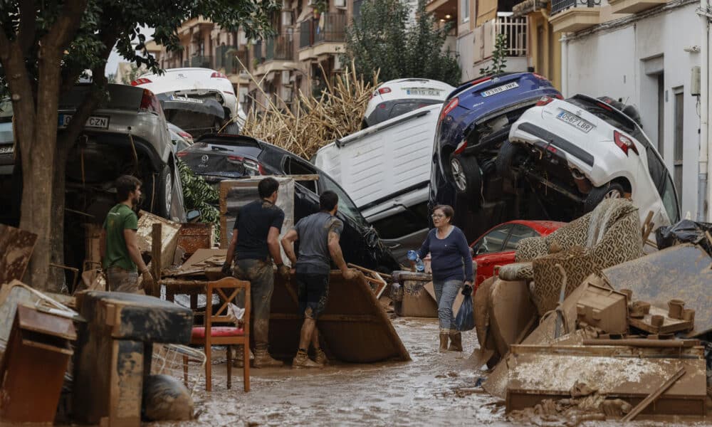 Vecinos de Paiporta trabajan en la limpieza de calles, locales y viviendas de la localidad junto a una montaña de vehículos arrastrados por la corriente, este viernes, en la provincia de Valencia (España). EFE/Biel Aliño