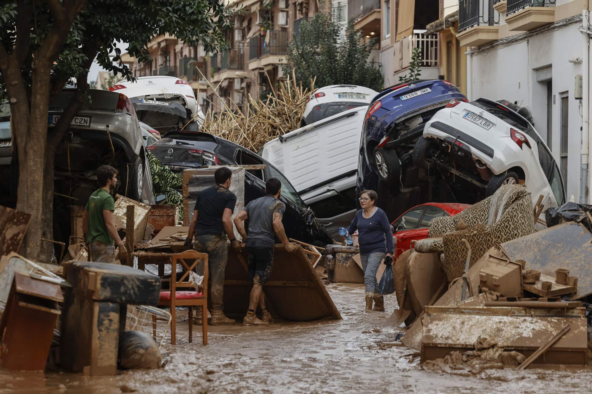 Vecinos de Paiporta trabajan en la limpieza de calles, locales y viviendas de la localidad junto a una montaña de vehículos arrastrados por la corriente, este viernes, en la provincia de Valencia (España). EFE/Biel Aliño