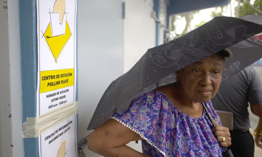 Una mujer se cubre de la lluvia esperando su turno para depositar su voto en un centro de votación en Carolina (Puerto Rico). EFE/Thais Llorca