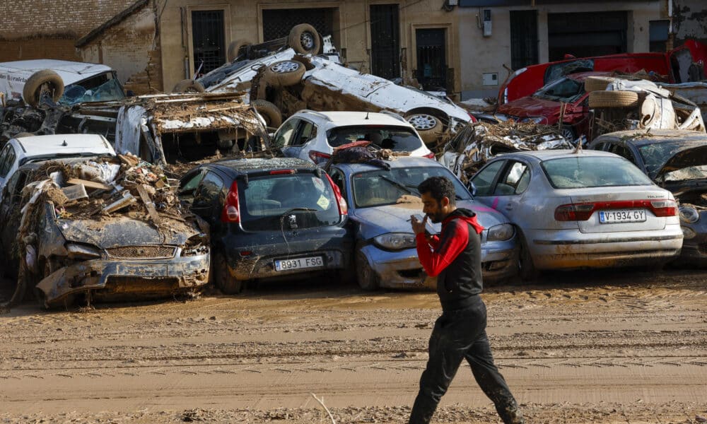 Un hombre camina junto a los coches apilados en Catarroja, Valencia este martes, una de las localidades más afectados por las inundaciones. EFE/ Chema Moya