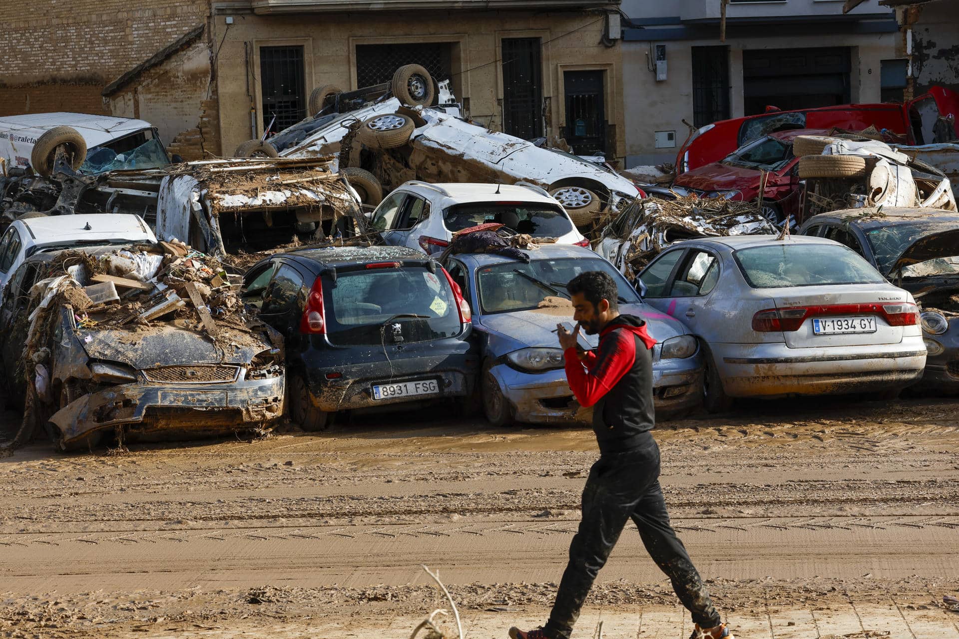 Un hombre camina junto a los coches apilados en Catarroja, Valencia este martes, una de las localidades más afectados por las inundaciones. EFE/ Chema Moya