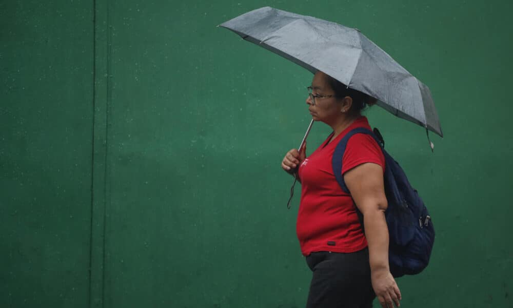 Fotografía de archivo en donde una mujer se protege de la lluvia en el centro de San Salvador (El Salvador). EFE/Rodrigo Sura