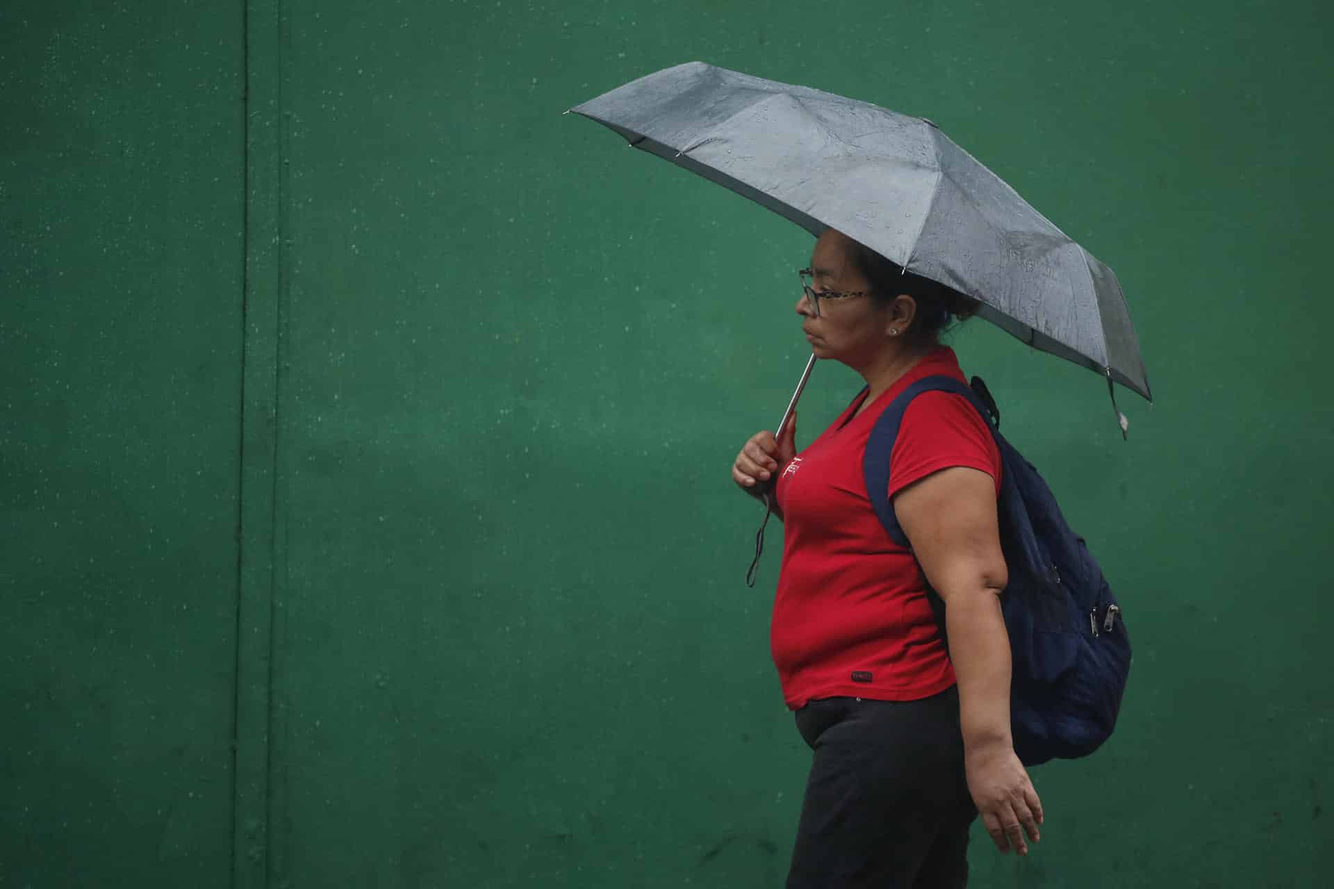 Fotografía de archivo en donde una mujer se protege de la lluvia en el centro de San Salvador (El Salvador). EFE/Rodrigo Sura