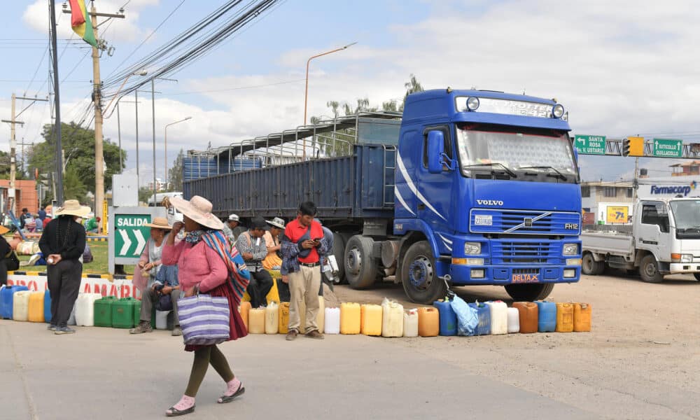 Una mujer Quechua camina delante de personas que hacen filas para comprar combustible en una estación de servicio este jueves en Cochabamba (Bolivia). EFE/Jorge Abrego