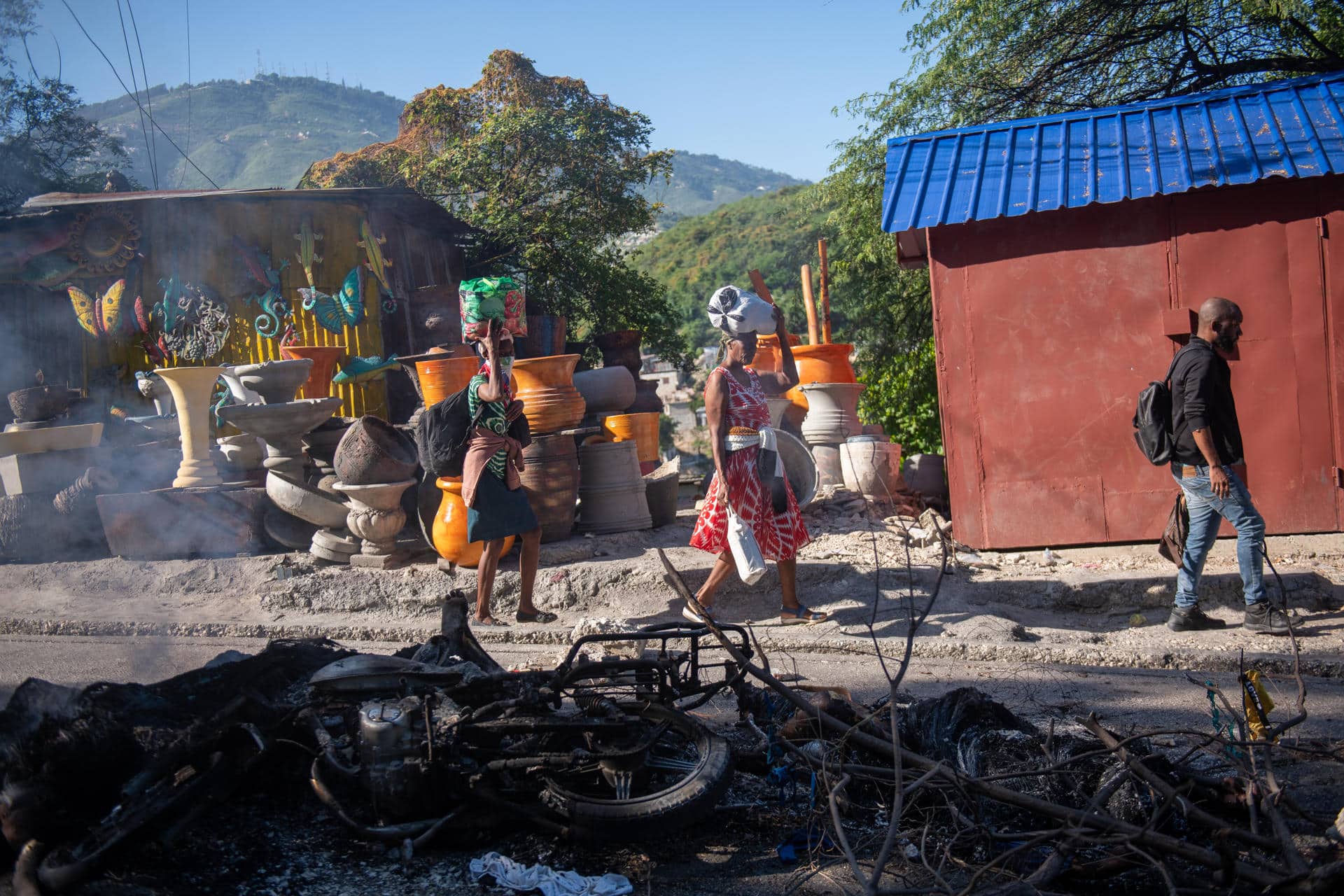 Personas pasan frente a los restos de una hoguera donde incineraron a un pandillero este martes, en una calle de Puerto Príncipe (Haití). EFE/ Johnson Sabin