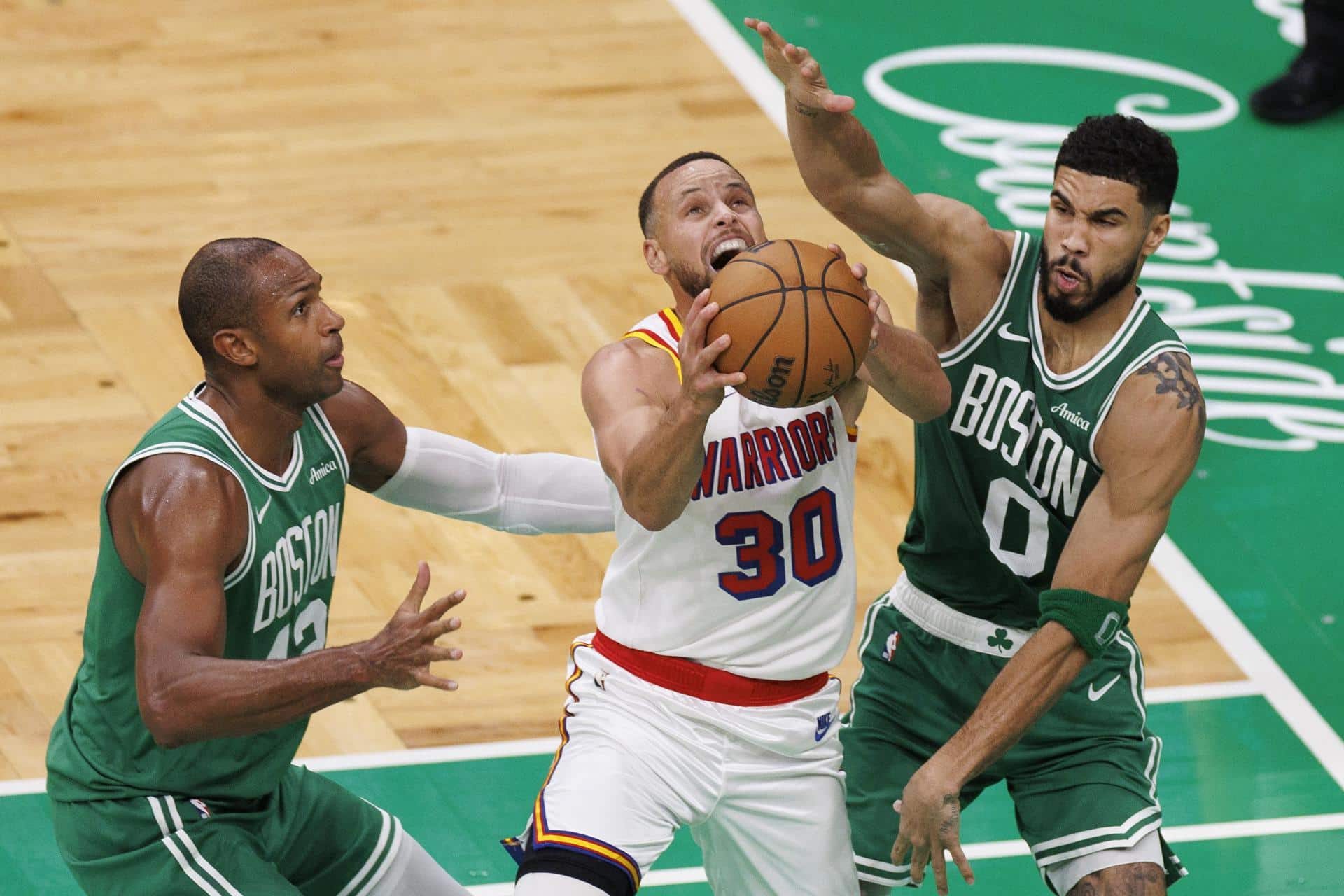 El escolta de los Golden State Warriors Stephen Curry (C) intenta anotar obstaculizado por el pívot de los Boston Celtics, Al Horford (I), y el ala-pívot Jayson Tatum (D) durante el partido de baloncesto de la NBA entre los Boston Celtics y los Golden State Warriors en Boston, Massachusetts. EFE/EPA/CJ GUNTHER SHUTTERSTOCK OUT