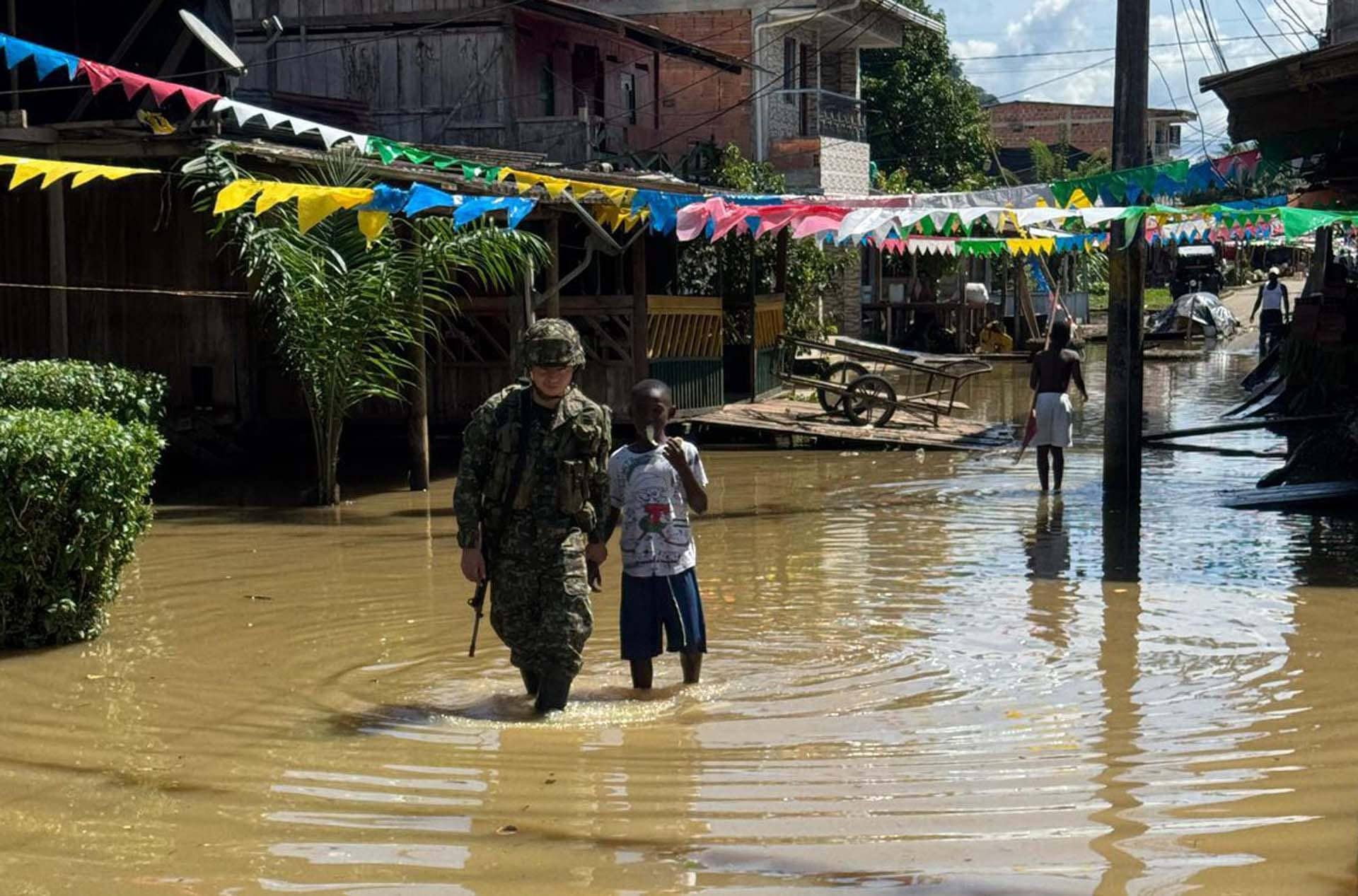 Fotografía cedida por el Ejército de Colombia que muestra a un solado acompañando a un joven por una calle inundada, en Alto Baudó (Colombia). EFE/Ejército de Colombia