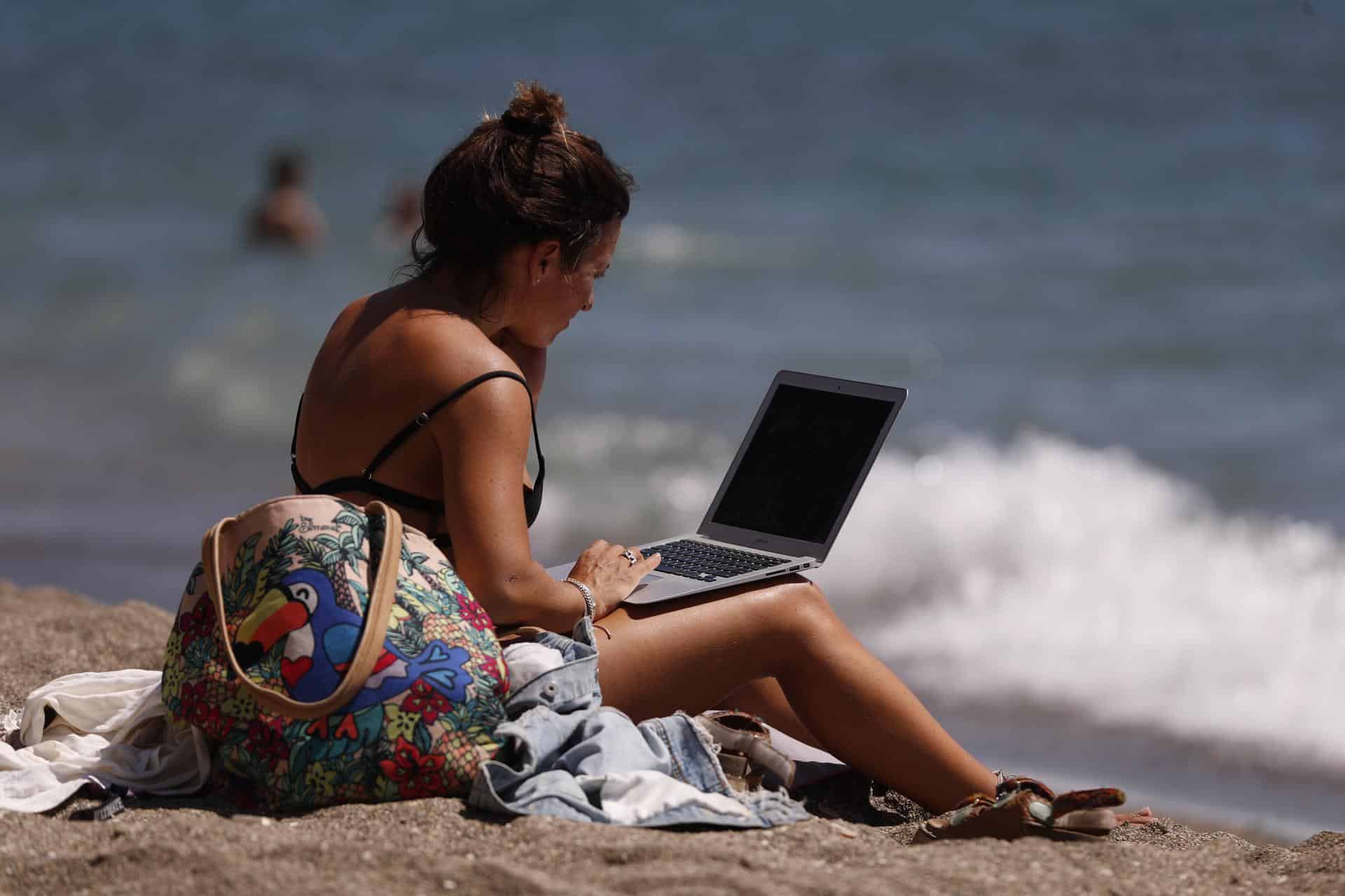 Una mujer toma el sol mientras mira su ordenador portátil. EFE/ Jorge Zapata/Archivo