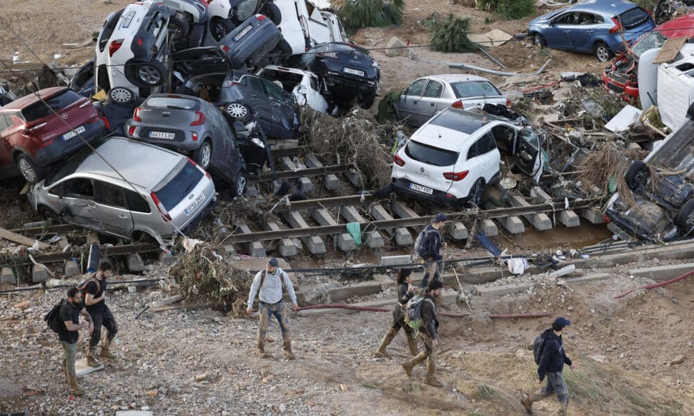 Varias personas caminan entre los vehículos apilados sobre las vías del tren en Alfafar (Valencia), este viernes. La búsqueda de desaparecidos, la identificación de víctimas mortales, las tareas de limpieza y la reparación de infraestructuras continúan tres días después de las inundaciones que han asolado la provincia de Valencia, en una jornada en la que el Gobierno envía a 500 militares más, que se sumarán a las 1.200 efectivos de la Unidad Militar de Emergencias (UME), para actuar en Utiel, Requena, Riba-roja, Torrent, Paiporta y Algemesí. EFE/ Kai Försterling