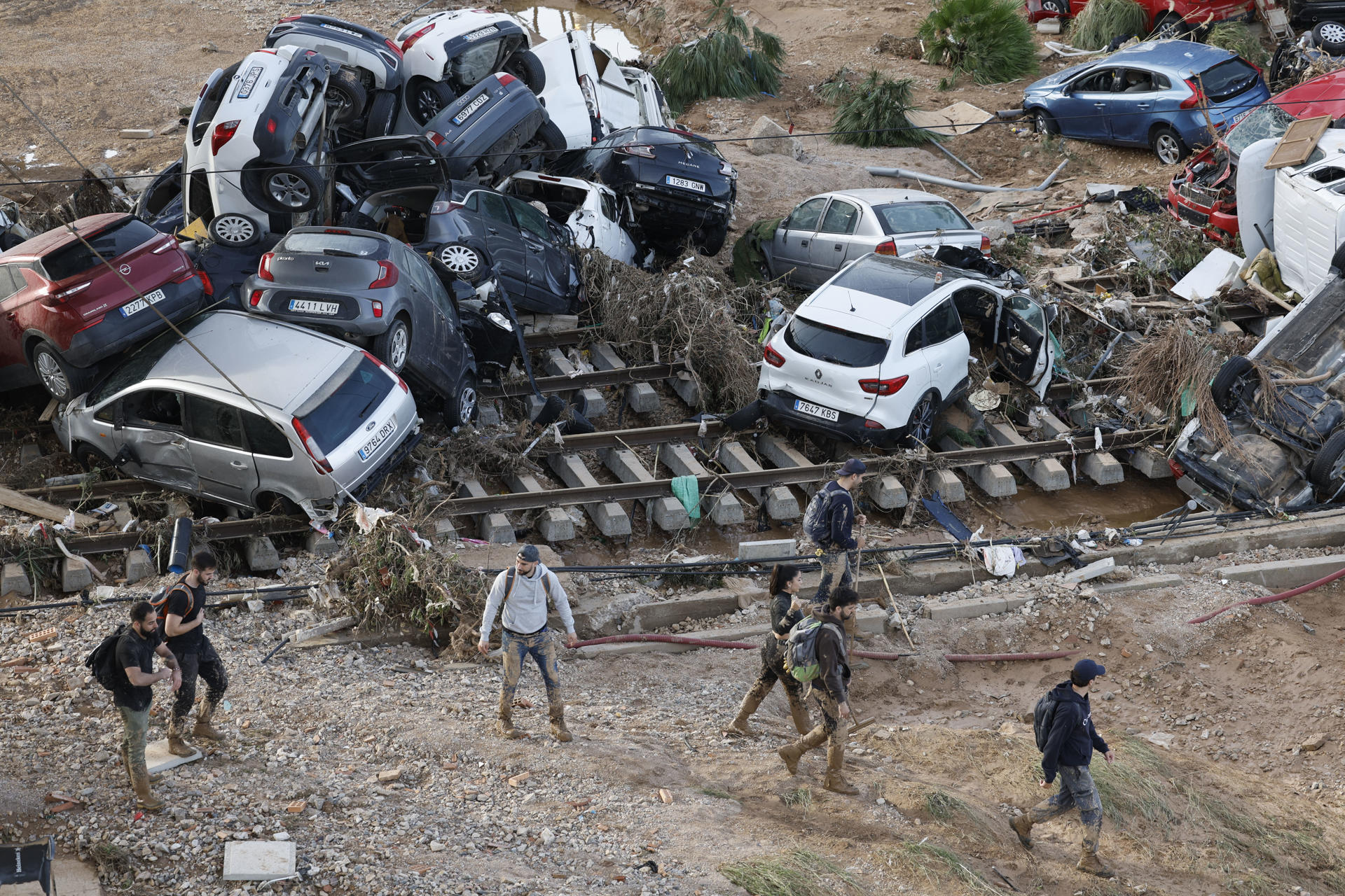 Varias personas caminan entre los vehículos apilados sobre las vías del tren en Alfafar (Valencia), este viernes. La búsqueda de desaparecidos, la identificación de víctimas mortales, las tareas de limpieza y la reparación de infraestructuras continúan tres días después de las inundaciones que han asolado la provincia de Valencia, en una jornada en la que el Gobierno envía a 500 militares más, que se sumarán a las 1.200 efectivos de la Unidad Militar de Emergencias (UME), para actuar en Utiel, Requena, Riba-roja, Torrent, Paiporta y Algemesí. EFE/ Kai Försterling