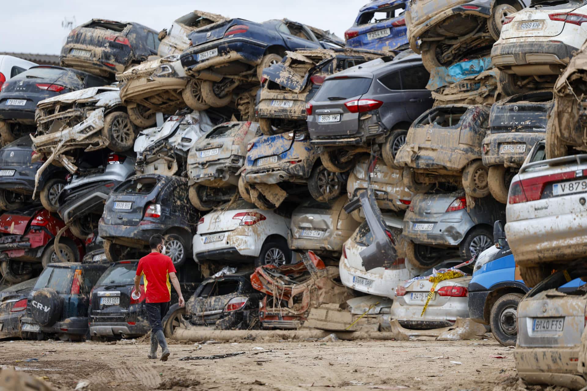 Un voluntario camina junto a una pila de vehículos destrozados en Paiporta, este martes. EFE/Jorge Zapata